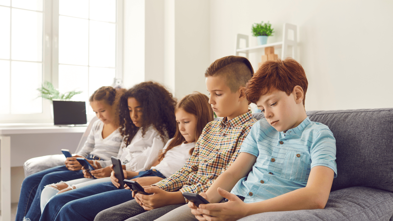 Gruppe von Kindern unterschiedlichen Alters, die konzentriert auf ihre Smartphones blicken, während sie nebeneinander auf einer Couch sitzen.